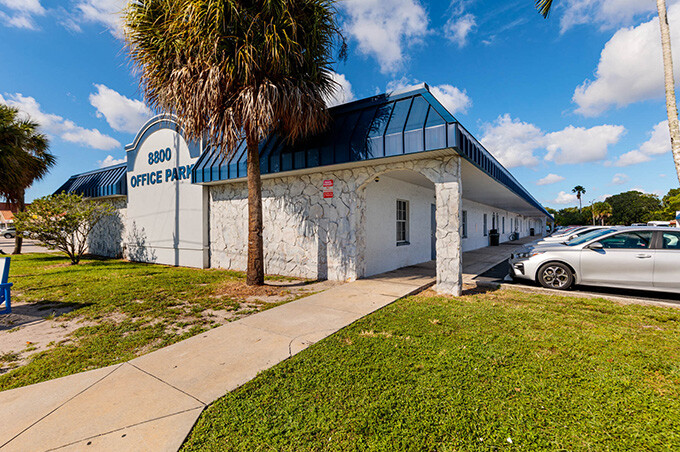 Exteriors from 8800 49th St N. A blue building with a cobblestone wall and palm trees out front.