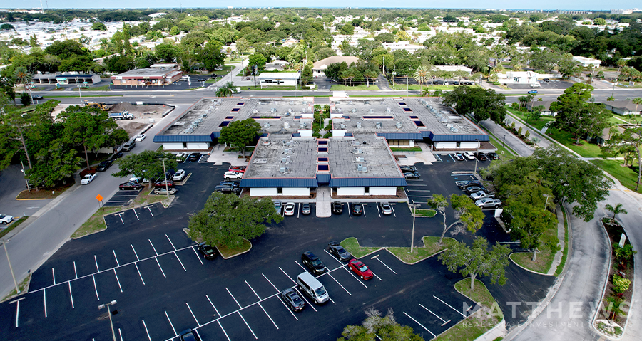 A group of 3 buildings with an expansive parking lot. Trees and grass are riddled throughout the lot